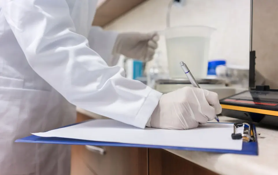 Regulation & Quality Control: Ensuring global compliance, safety, and certified sustainability. Scientist in a lab coat writing on a clipboard while conducting quality control tests, representing InnuScience's dedication to regulation and certified sustainability.